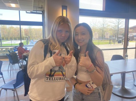 Two girls giving a thumbs up to the camera in a cafeteria.