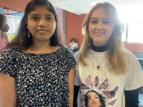 Two High school girls standing next to each other in a crowded area.